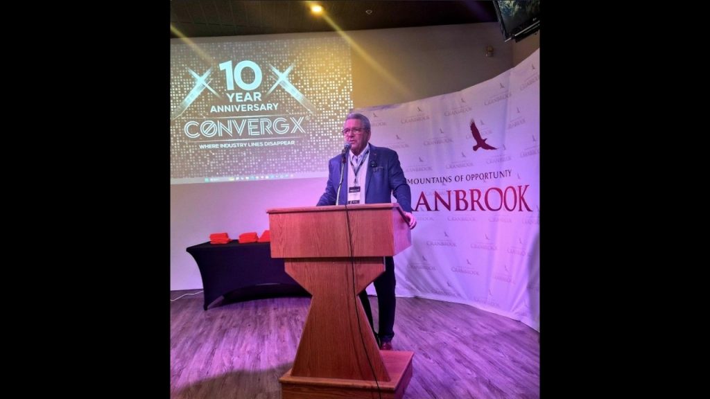 ConvergX Cranbrook: a speaker at a lectern in front of a City of Cranbrook backdrop, beside a projected ConvergX tenth anniversary slide.